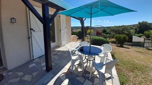 An outdoor patio with a table and chairs under a blue umbrella, a white door, and a view of the countryside. - Cozy House with Garden near Thermes du Connétable - 2 BR, Fully Equipped, WiFi, Sleeps 4 (La Roche-Posay)