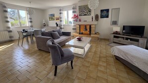 A modern living room with a sofa, armchair, dining table, and fireplace. - Cozy House with Garden near Thermes du Connétable - 2 BR, Fully Equipped, WiFi, Sleeps 4 (La Roche-Posay)