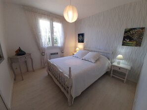 A bedroom with a large bed, two bedside tables with lamps, a window with curtains, and a wall with a textured pattern.