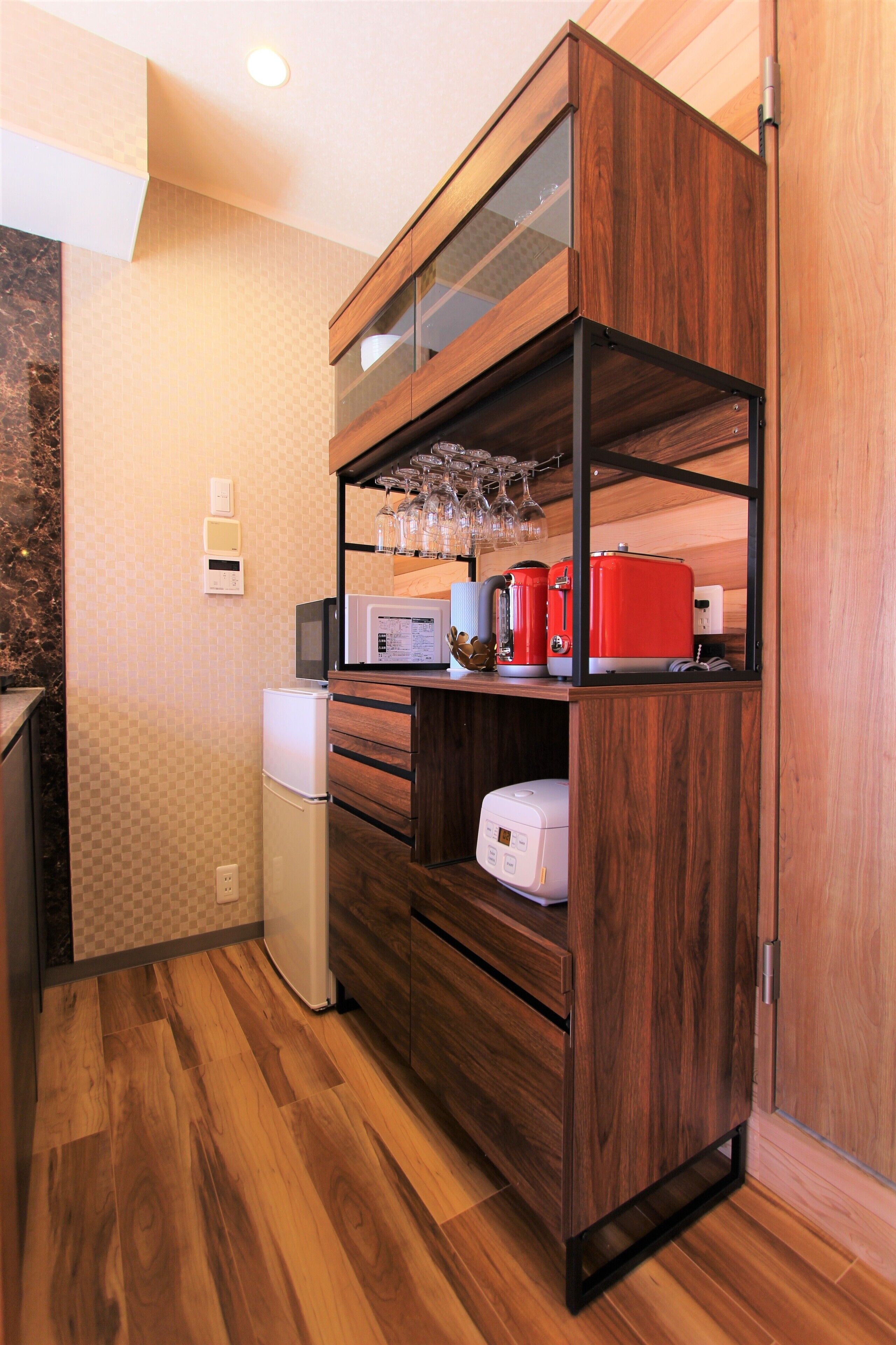 A compact kitchen with wooden cabinetry, a microwave, a red toaster, and a small refrigerator.