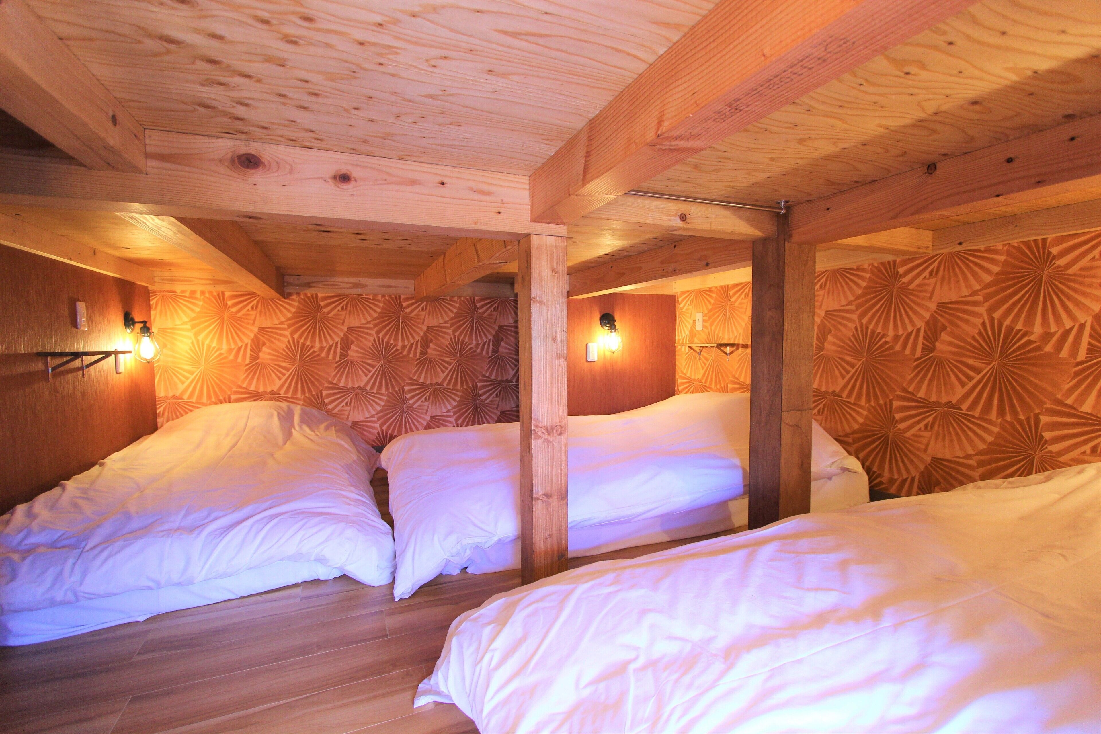 A room with three beds, wooden beams, and patterned wallpaper.