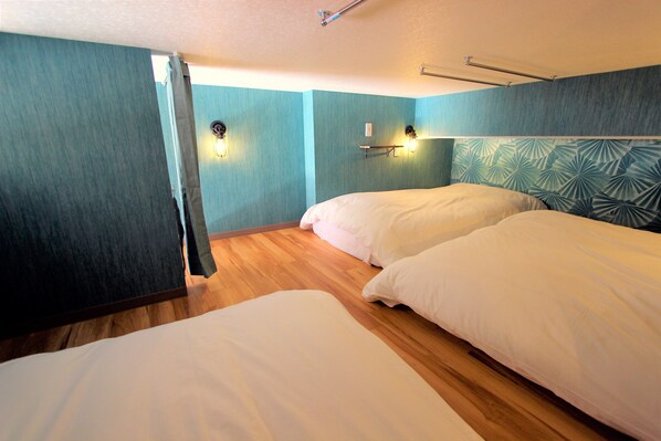 Un dormitorio con dos camas, suelo de madera, paredes color turquesa e iluminación empotrada.