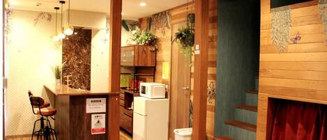 A compact hotel room with a kitchenette, wooden accents, a small seating area, and a view of the outside.