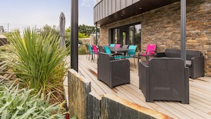 Eine Terrasse im Freien mit Korbmöbeln, einer Steinmauer und einer Metall-Dachkonstruktion.