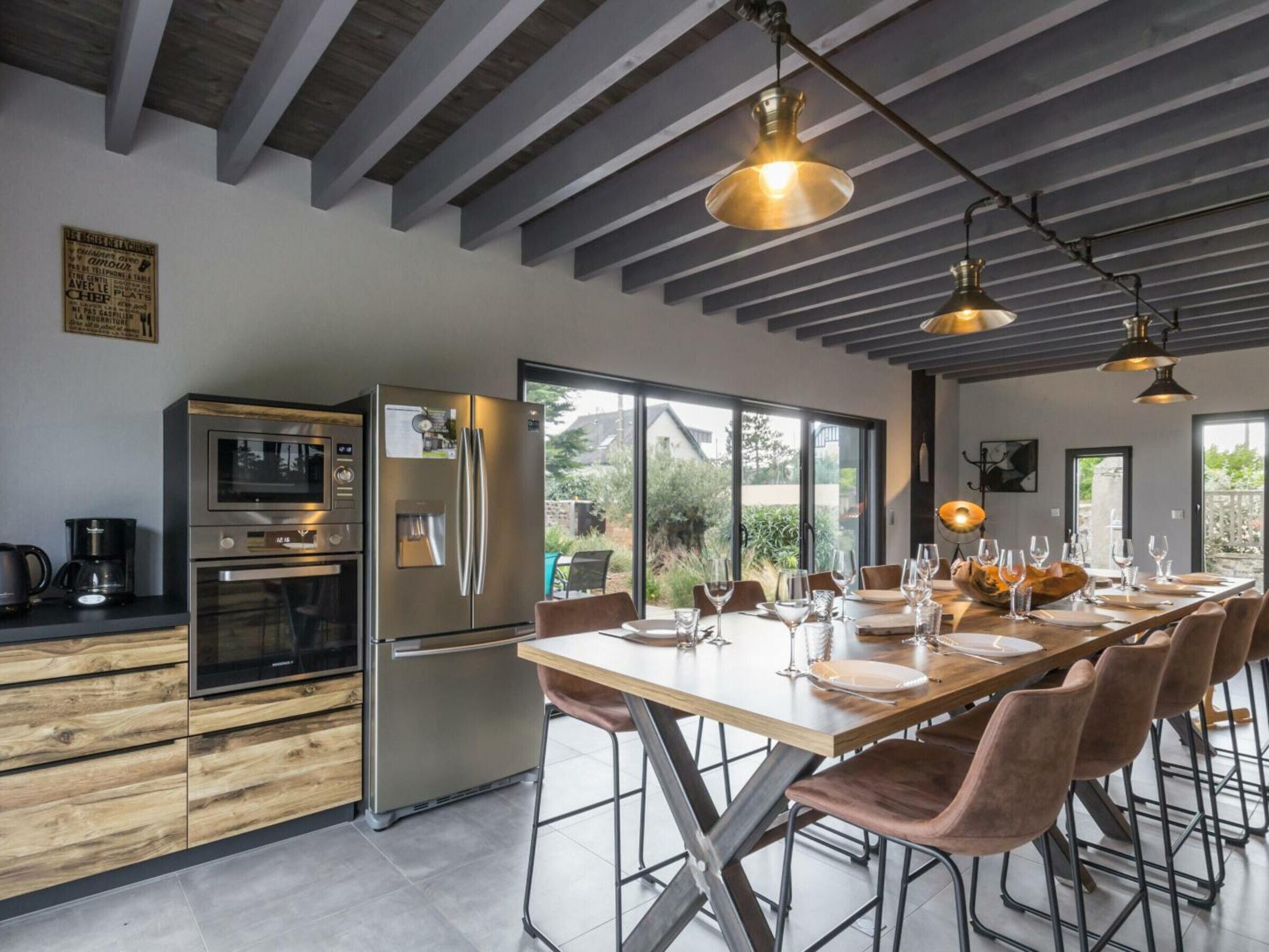 Una cucina moderna con elettrodomestici in acciaio inossidabile, un'area pranzo con un tavolo lungo e sedie, e ampie finestre che offrono vista sull'esterno.