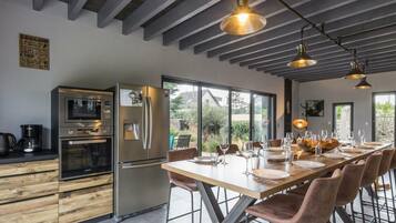 Una cucina moderna con elettrodomestici in acciaio inossidabile, un'area pranzo con un tavolo lungo e sedie, e ampie finestre che offrono vista sull'esterno.