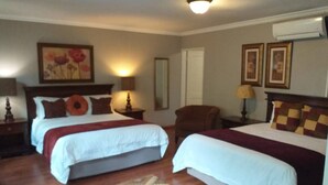 A hotel room with two beds, a wooden floor, a patterned rug, and a painting on the wall. - Fatmols lodge (Ndola)