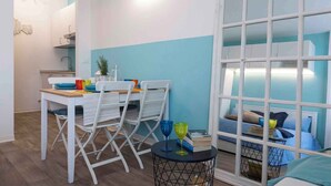 A compact room with a dining area, a small table with chairs, a bed with a headboard, and a window with blinds. - Studio mit Klimaanlage und Meerblick (Porto Santa Margherita)