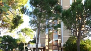 A modern multi-story building with a central tower, surrounded by trees and a well-maintained lawn. - Studio mit Klimaanlage und Meerblick (Porto Santa Margherita)