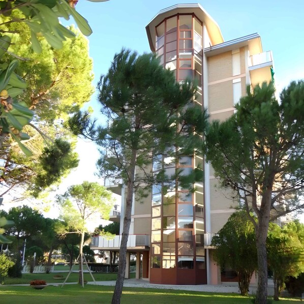 A modern multi-story building with a central tower, surrounded by trees and a well-maintained lawn.