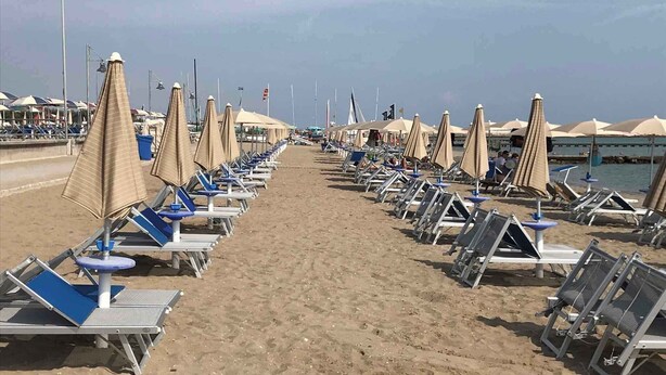 A beach with rows of sun loungers and umbrellas, a clear sky, and a calm sea. - Studio mit Klimaanlage und Meerblick (Porto Santa Margherita)