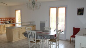 Un coin repas avec une table dressée pour quatre personnes, entourée de chaises blanches. On y trouve également un coin cuisine avec un micro-ondes et des placards sur le côté gauche.