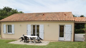 Un bâtiment avec un toit en tuiles, une porte et une table entourée de chaises au premier plan.
