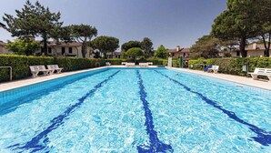 Une piscine rectangulaire à l’eau d’un bleu cristallin, entourée de chaises longues blanches et de verdure.