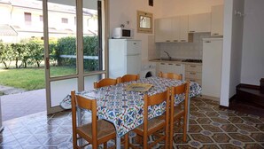 Une cuisine de taille réduite avec des meubles blancs, un four à micro-ondes et un évier. On y trouve une table à manger avec des chaises et une nappe à motifs.