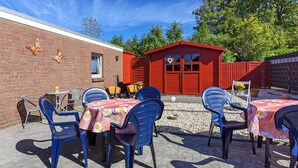 An outdoor patio with blue plastic chairs and tables, a red shed, and a brick wall with butterfly decorations. - Ferienwohnung 2 im Ferienhaus Trautes Heim - Ferienwohnung 2 (Esens)