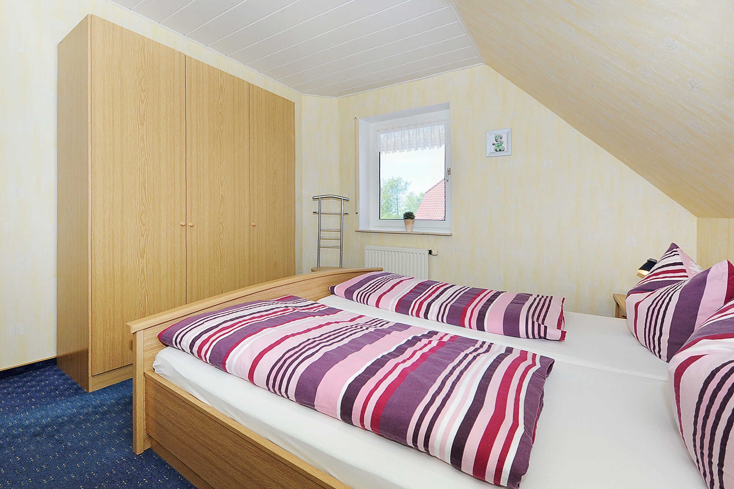 A bedroom with two beds, a wooden wardrobe, a window with a view, and a radiator.