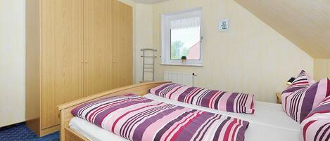 A bedroom with two beds, a wooden wardrobe, a window with a view, and a radiator.