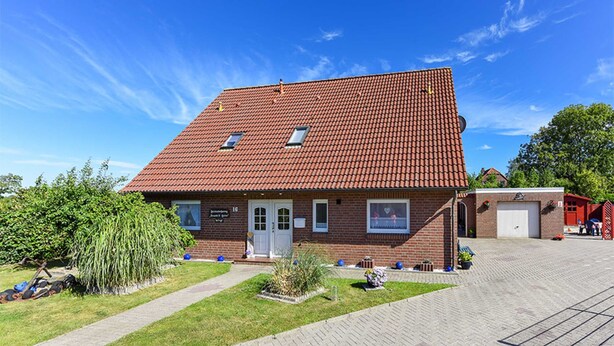A two-story building with a red-tiled roof, a front entrance, and a small garden area with a pathway leading to the entrance. - Ferienwohnung 2 im Ferienhaus Trautes Heim - Ferienwohnung 2 (Esens)