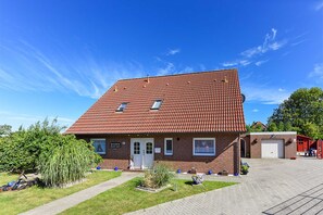 A two-story building with a red-tiled roof, a front entrance, and a small garden area with a pathway leading to the entrance. - Ferienwohnung 2 im Ferienhaus Trautes Heim - Ferienwohnung 2 (Esens)