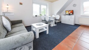 A compact living space with a sofa, a small dining table with chairs, a TV, and a clock on the wall. - Ferienwohnung 2 im Ferienhaus Trautes Heim - Ferienwohnung 2 (Esens)