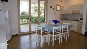 A kitchen with a dining table, white cabinets, a refrigerator, and a window with a view of greenery. - Holiday home with outdoor swimming pool and terrace (Porto Santa Margherita)