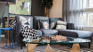 A modern living room with a glass coffee table, a grey sofa with patterned cushions, a blue chair, and a large plant. - Sky Mark Lux 2 - Seattle's Best Modern 3BD HomeTel (Seattle)