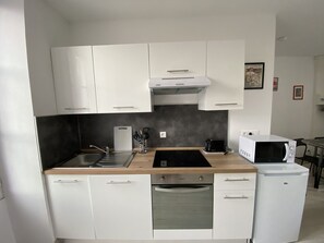 Cocina compacta con armarios blancos, microondas, tostadora y lavavajillas.