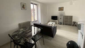 A modern room with a dining table, black sofa, TV, and a white cabinet.