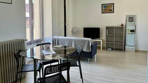 A modern living room with a glass dining table, a sofa, a TV, and a refrigerator.