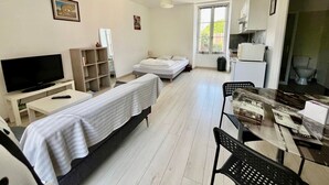 A room with a bed, a TV, a desk, a chair, a small table, and a window.