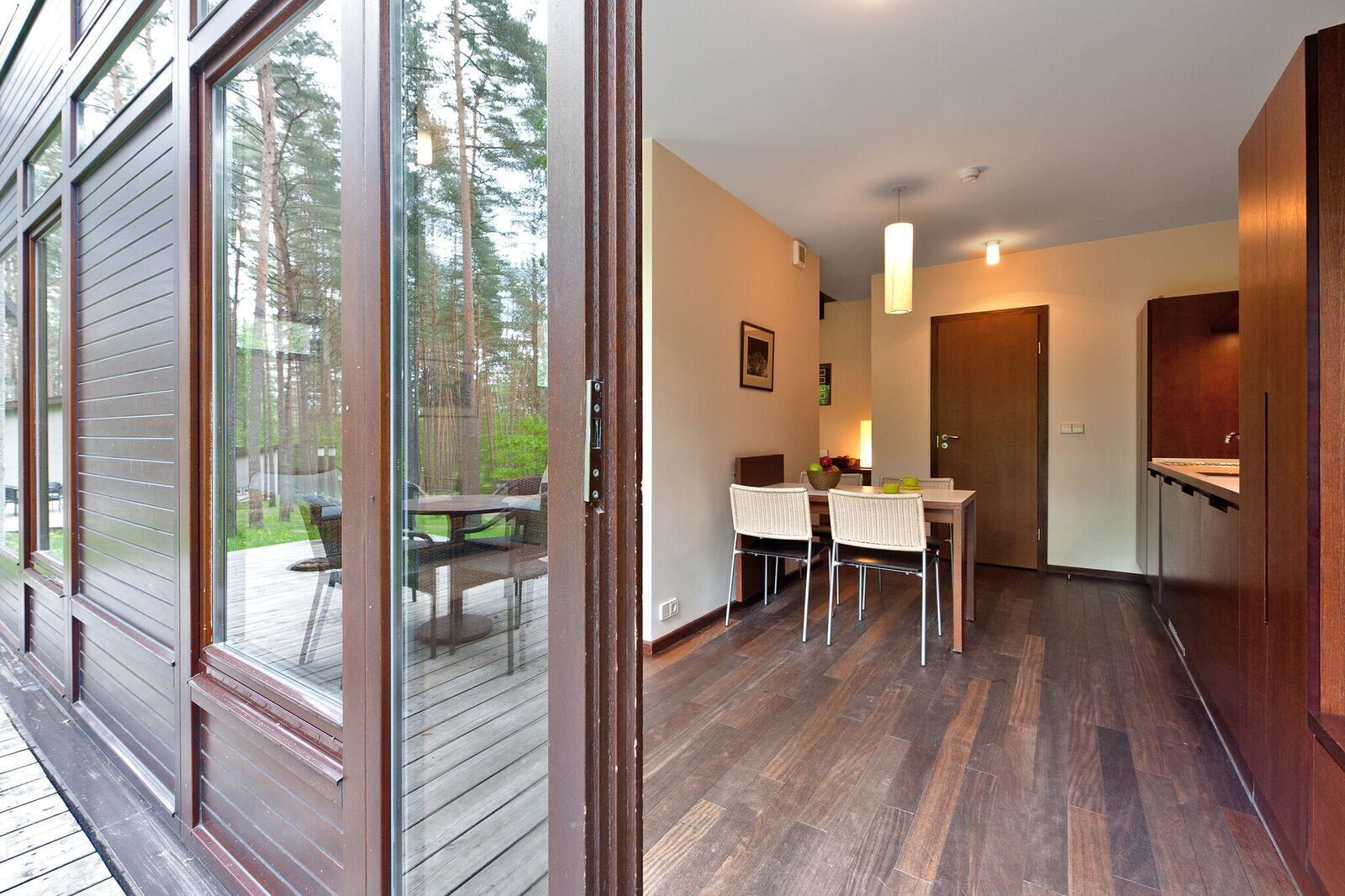 Et moderne interiør med et træbord, to stole, et køkken og udsigt til en terrasse med havemøbler.