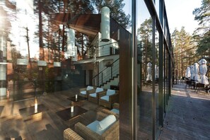 A modern interior with a glass wall, wicker furniture, and a staircase leading to an upper level. - SPA Hotel Belvilis (Moletai)