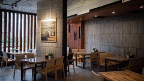 A modern dining area with wooden tables and chairs, a large painting on the wall, and large windows allowing natural light. - YZ Spa house (Jiaoxi)