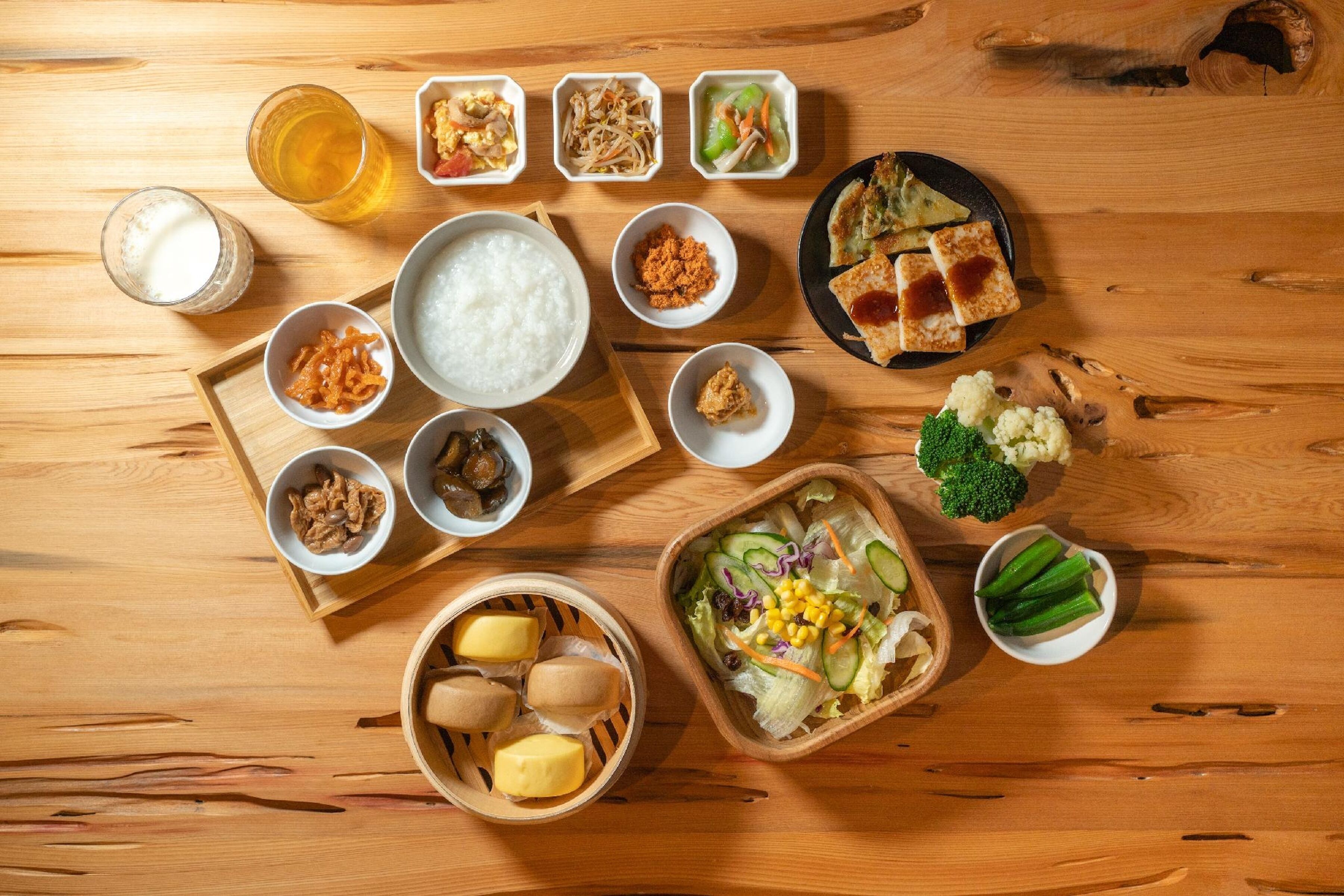 Une table en bois sur laquelle on trouve différents plats, notamment du riz, des légumes et une salade.