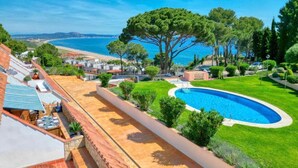 A pool surrounded by a well-maintained lawn, a large tree, and a view of the sea.