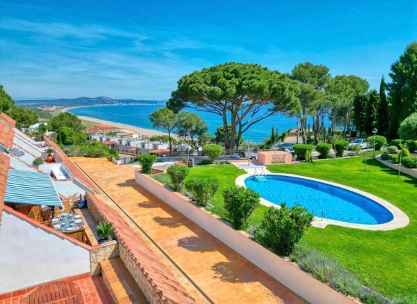 A pool surrounded by a well-maintained lawn, a large tree, and a view of the sea.