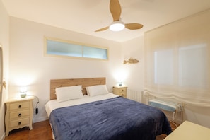 A bedroom with a bed, bedside tables, a ceiling fan, a window with blinds, and a radiator.