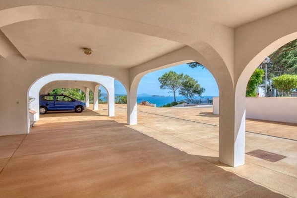 Un vaste espace abrité où une voiture est garée sous une arche, donnant accès à une vue panoramique sur la mer.