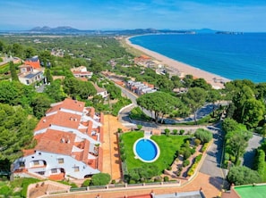 Vue aérienne d’un quartier résidentiel situé sur la côte, avec une piscine, des maisons et une plage.