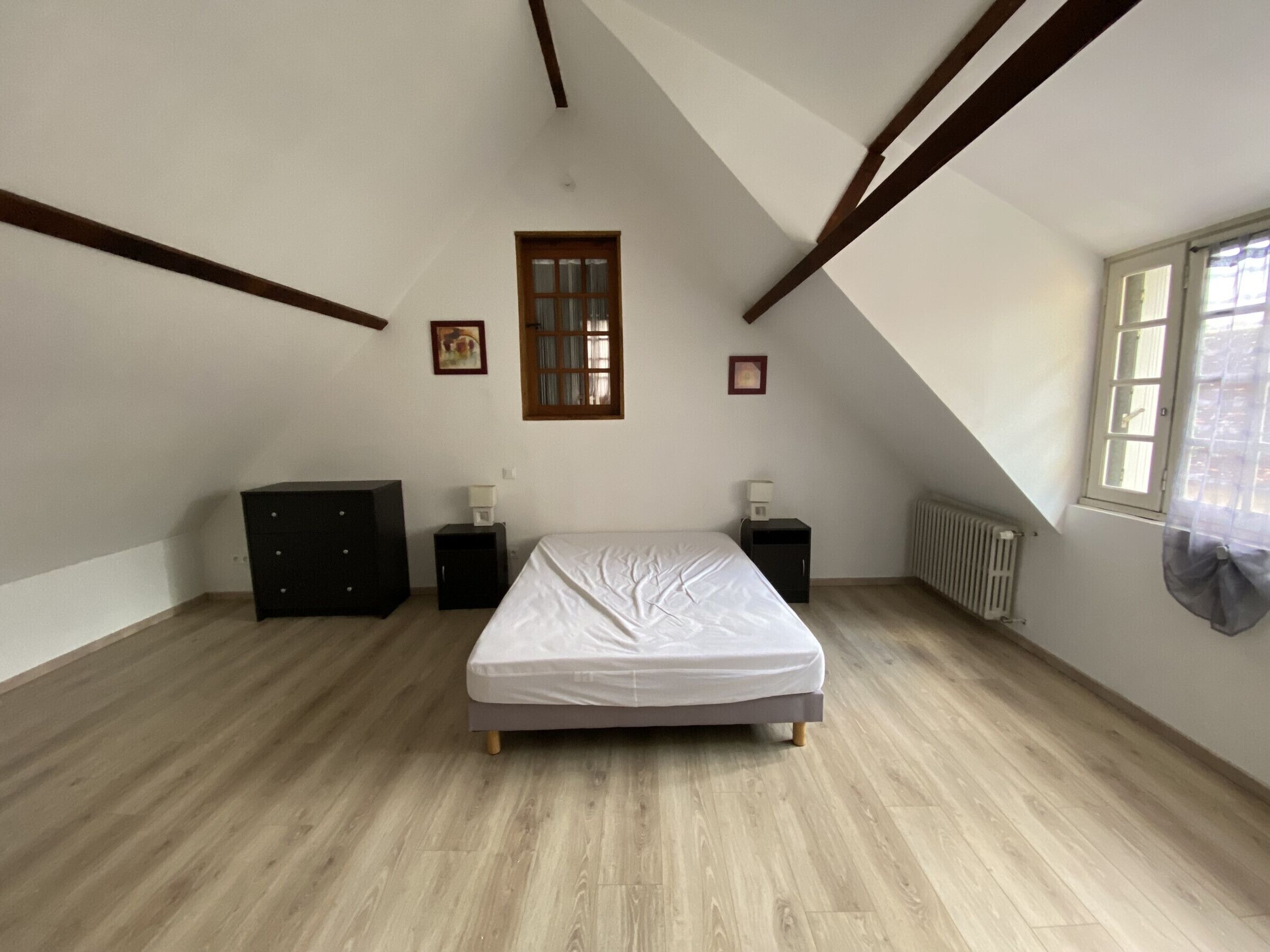 A bedroom with a bed, a dresser, a nightstand, a window, and a radiator.