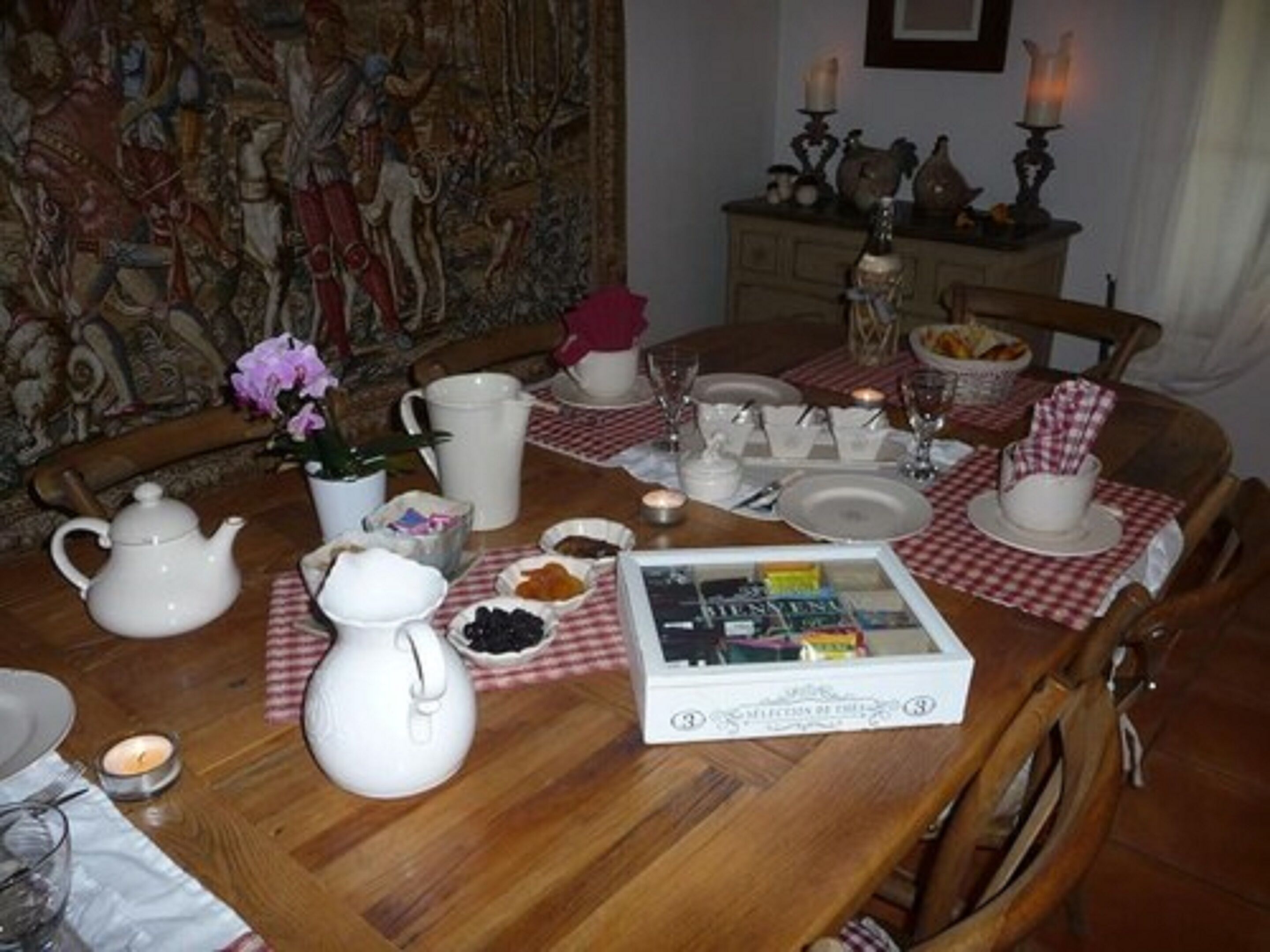 A dining table set with white teapots, pitchers, and plates, with a checkered tablecloth.