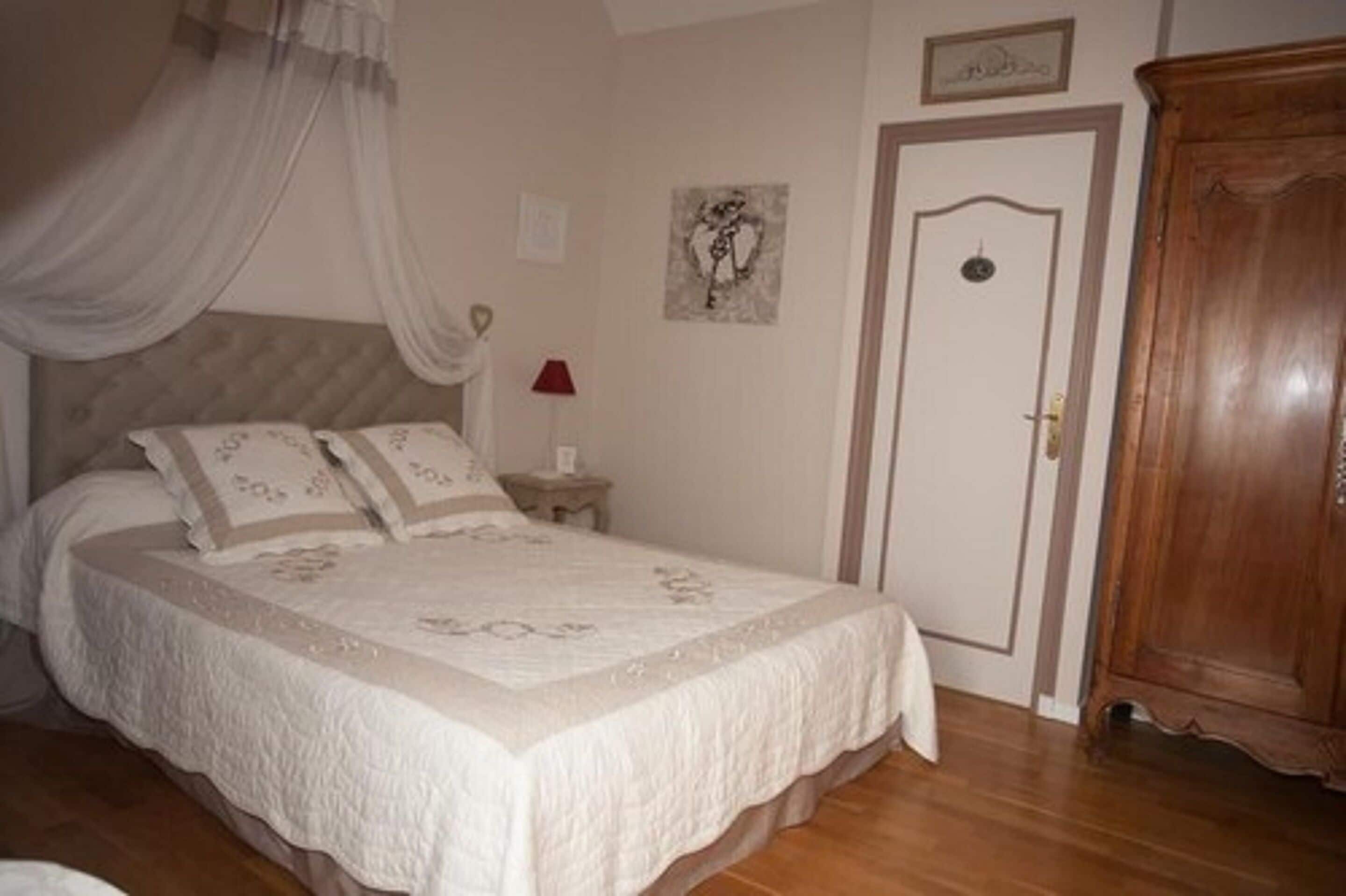 A bedroom with a bed, a nightstand, a wooden wardrobe, a door, and a wall-mounted picture.