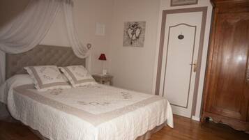 A bedroom with a bed, a nightstand, a wooden wardrobe, a door, and a wall-mounted picture.