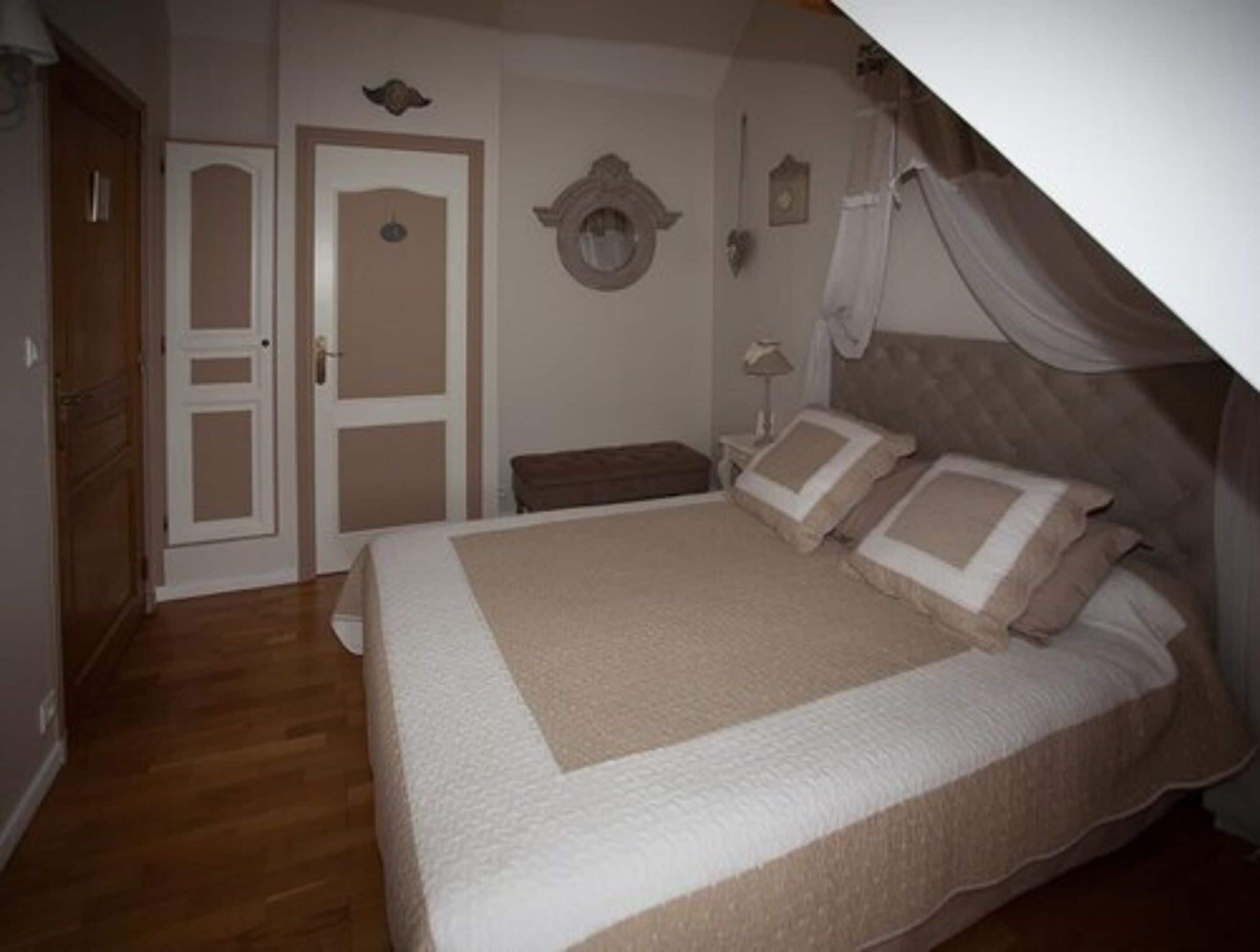 A bedroom with a large bed, a wooden wardrobe, a door, and a wall-mounted mirror.