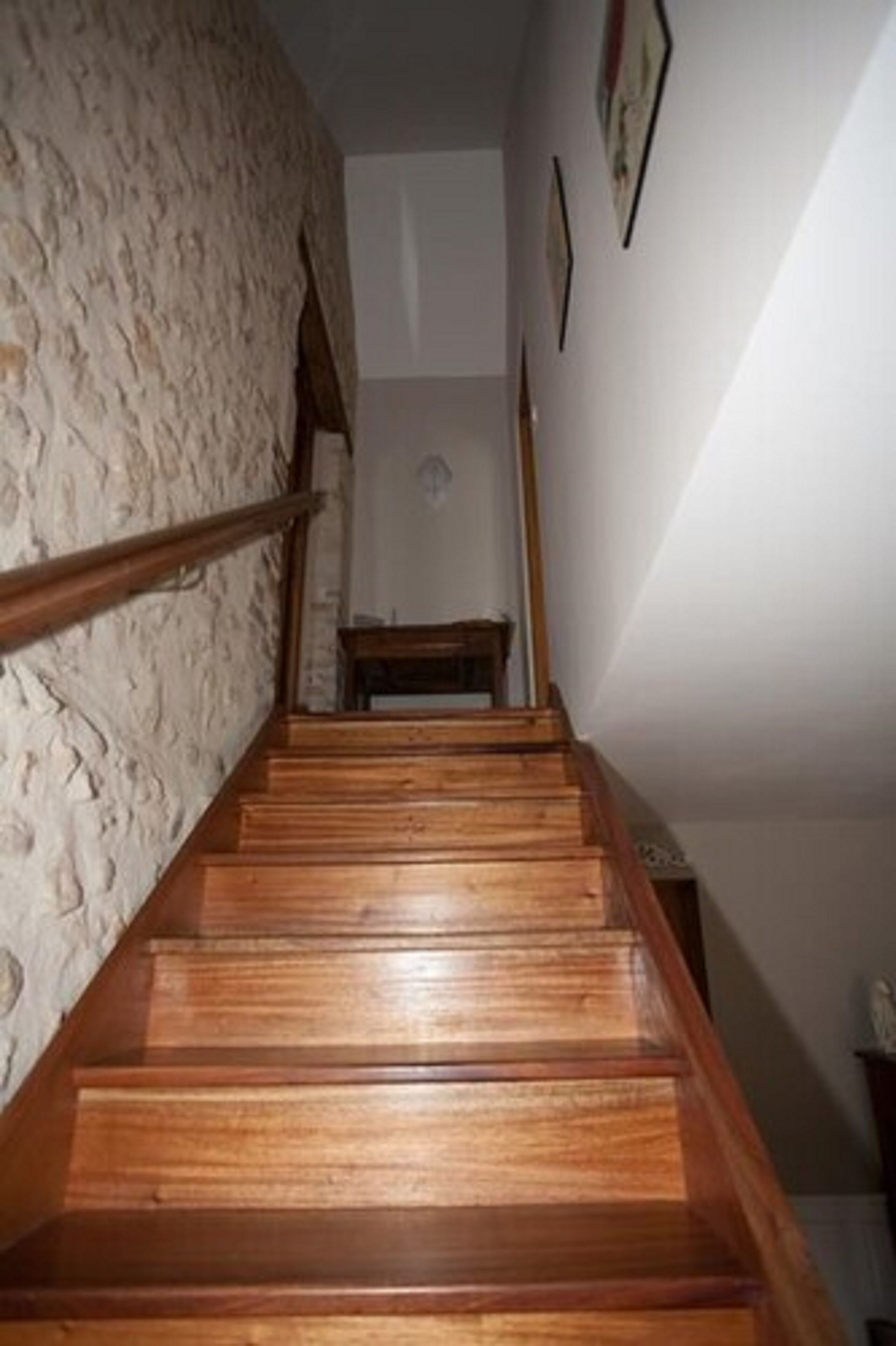 A wooden staircase with a textured wall on one side and framed pictures on the adjacent wall.