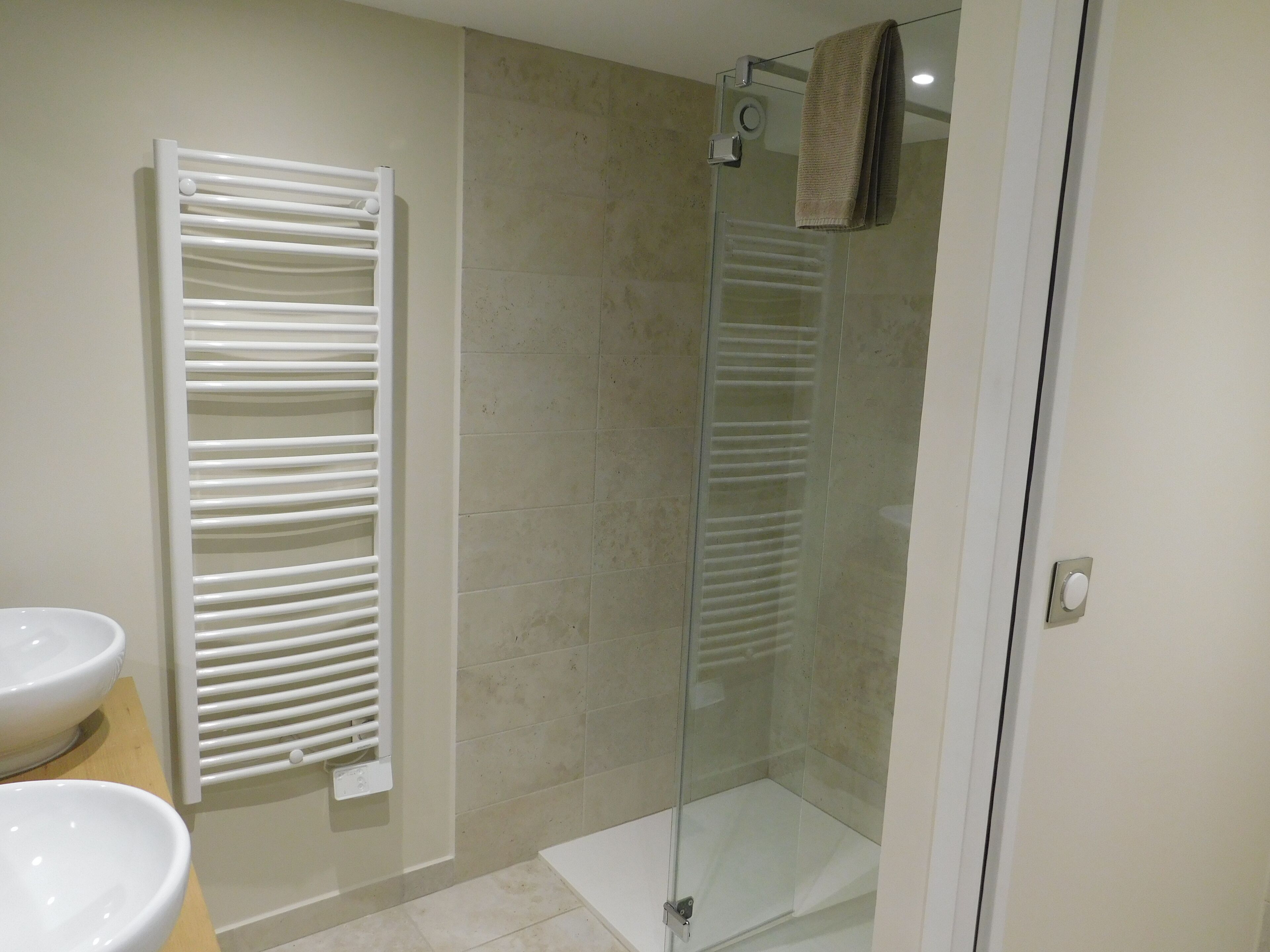 A bathroom with a glass shower enclosure, a white towel rack, and two white sinks.
