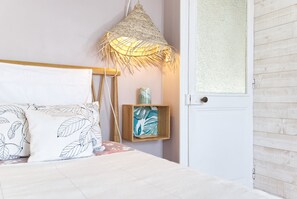 Un dormitorio con cama, lámpara colgante, estante de madera con un jarrón y una puerta con panel de vidrio esmerilado.