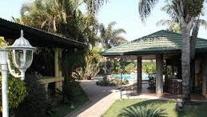 A pathway leading to a gazebo with a tiled roof, surrounded by palm trees and well-maintained grass. - Chabanga Lodge (Ndola)