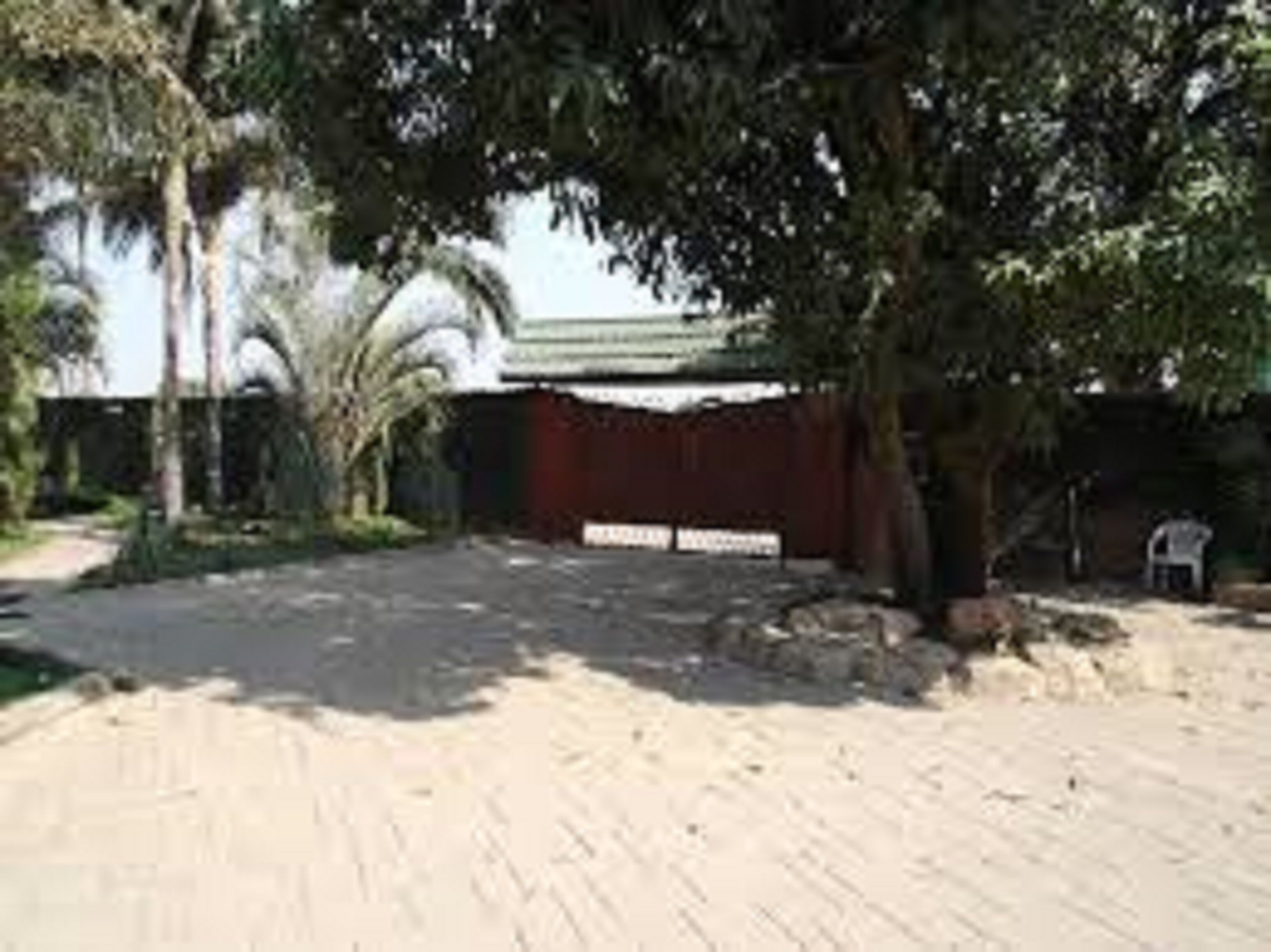 A paved courtyard with a red building, palm trees, and a white sign.